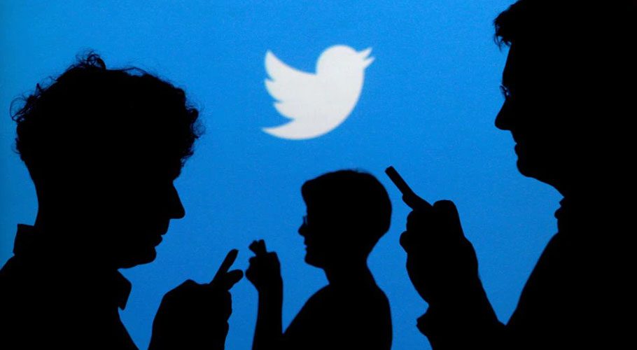 People holding mobile phones are silhouetted against a backdrop projected with the Twitter logo. Source: Reuters.