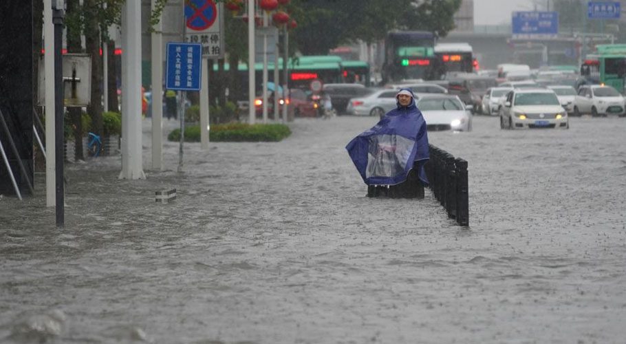 A resident wearing a rain cover stands on a flooded road in Zhengzhou, Henan province: Source Reuters.