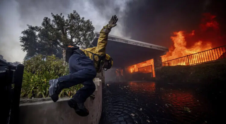 A firefighter jumps over a fence while fighting the Palisades Fire in the Pacific Palisades neighborhood of Los Angeles, Tuesday, Jan. 7, 2025. (AP Photo/Ethan Swope)