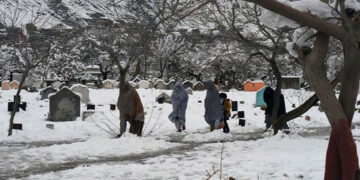 People walk past graves after heavy snowfall. — AFP/File