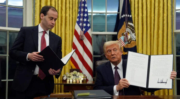 President Donald Trump holds up an executive order commuting sentences for people convicted of January 6 offences, in the Oval Office of the White House, Monday, January 20, 2025, in Washington, DC [Evan Vucci/AP]