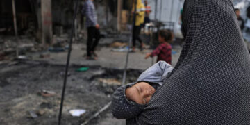 A Palestinian woman holds a child, as Palestinians inspect the damage at a school sheltering displaced people, following an Israeli strike, in Gaza City, April 23, 2025. REUTERS/Dawoud Abu Alkas