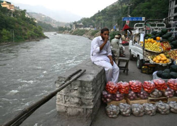 A fruit vendor sits on his stall alongside Jhelum River in Muzaffarabad.–AFP